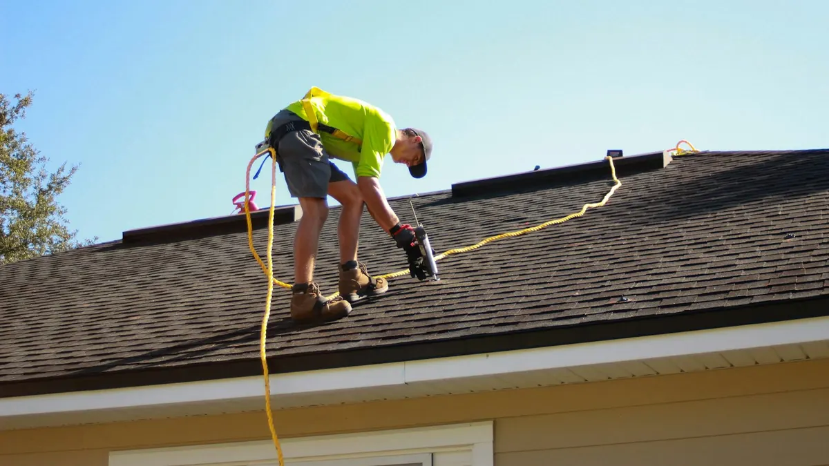 Roofer fixing shingles on a house roof with a power tool