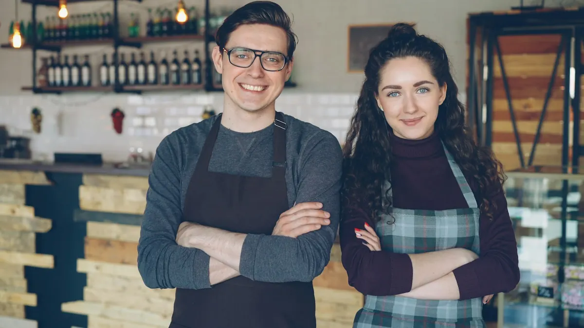 Two smiling café owners standing together in their shop