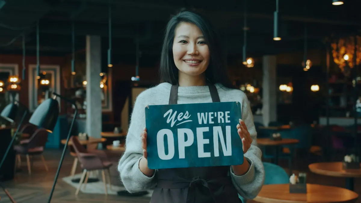 Café owner holding an “Open” sign behind the counter